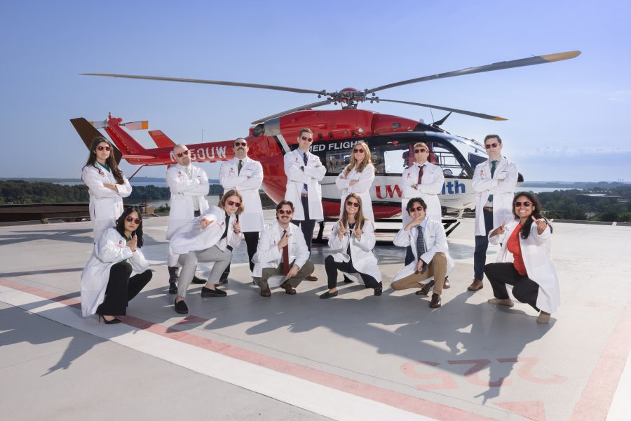 Residents wearing white coats pose playfully in front of a Med Flight helicopter.