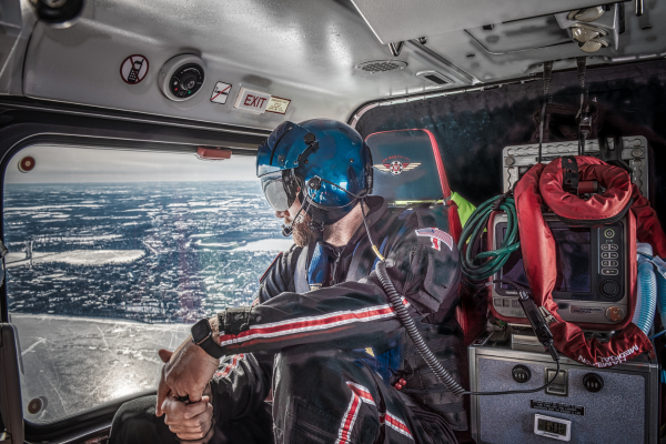 A flight physician, wearing a flight suit and helmet, looks out the helicopter window during a Med Flight transport.