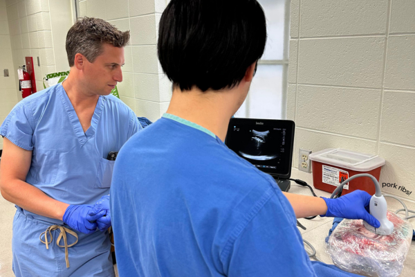 A resident practices ultrasound skills while a faculty member looks on, ready to give feedback.