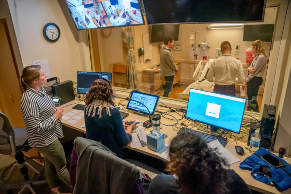 Three people in a control room observe a live simulation training at the UW Clinical Simulation Program.
