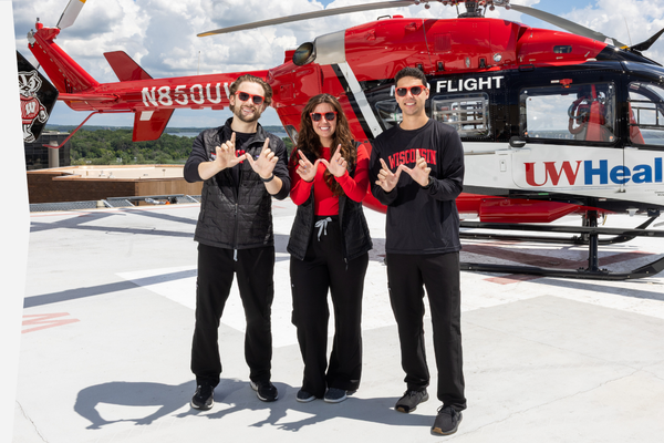 The three chief residents pose in front of a Med Flight helicopter wearing sunglasses and black and red University of Wisconsin clothing.