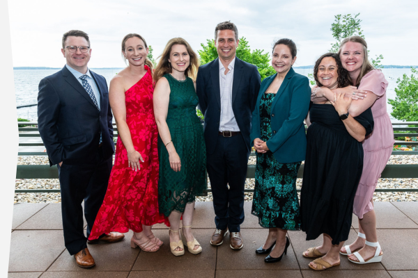 Residency Program Directors dressed in formal attire pose on an outdoor terrace overlooking a lake.